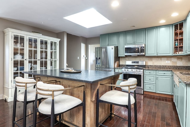 kitchen with dark countertops, a skylight, glass insert cabinets, stainless steel appliances, and dark wood-type flooring