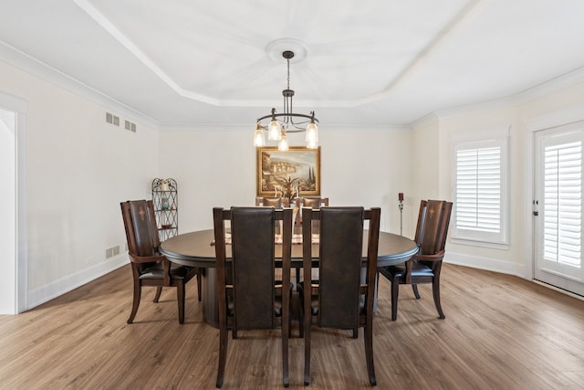 dining space with an inviting chandelier, a raised ceiling, visible vents, and wood finished floors