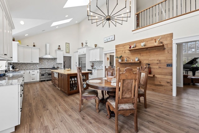 dining area featuring an inviting chandelier, wood finished floors, high vaulted ceiling, a skylight, and recessed lighting