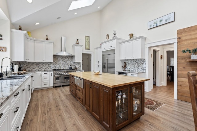 kitchen with a sink, a skylight, high vaulted ceiling, wall chimney exhaust hood, and high end appliances
