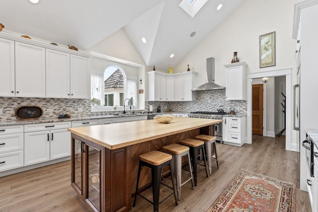 kitchen with a sink, high end stove, a skylight, butcher block countertops, and wall chimney range hood