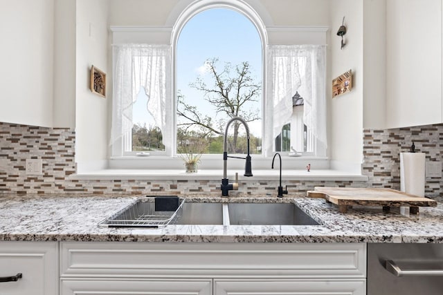details featuring a sink, white cabinetry, decorative backsplash, stainless steel dishwasher, and light stone countertops