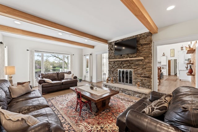living room with beamed ceiling, a stone fireplace, recessed lighting, and wood finished floors