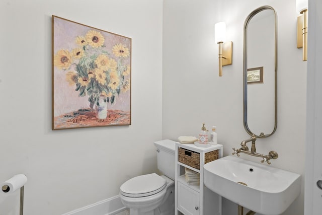 half bath with toilet, baseboards, and a sink