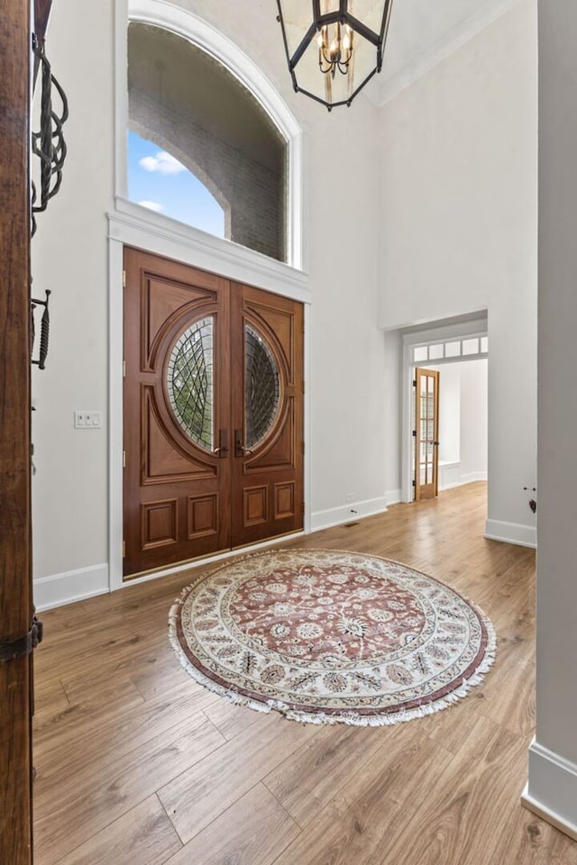 entryway featuring baseboards, ornamental molding, a chandelier, wood finished floors, and a high ceiling