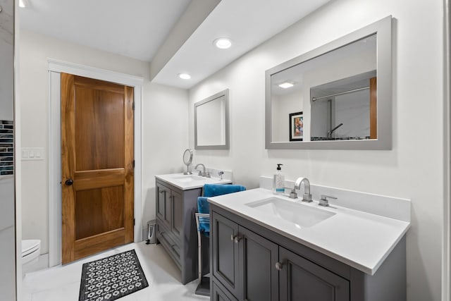 bathroom with two vanities, toilet, recessed lighting, and a sink
