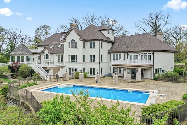 back of property featuring a fenced in pool, stucco siding, a chimney, and a balcony