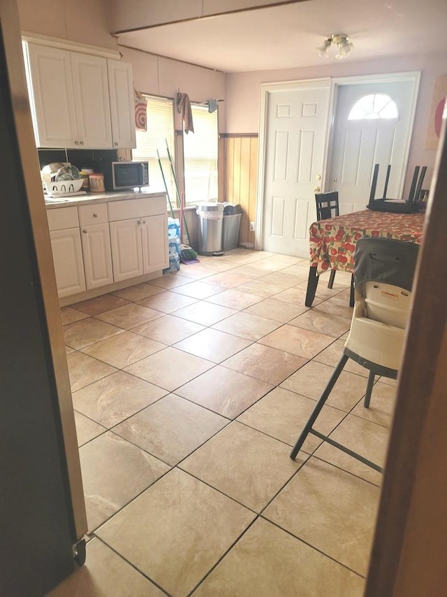 kitchen featuring light countertops, backsplash, white cabinetry, light tile patterned floors, and stainless steel microwave