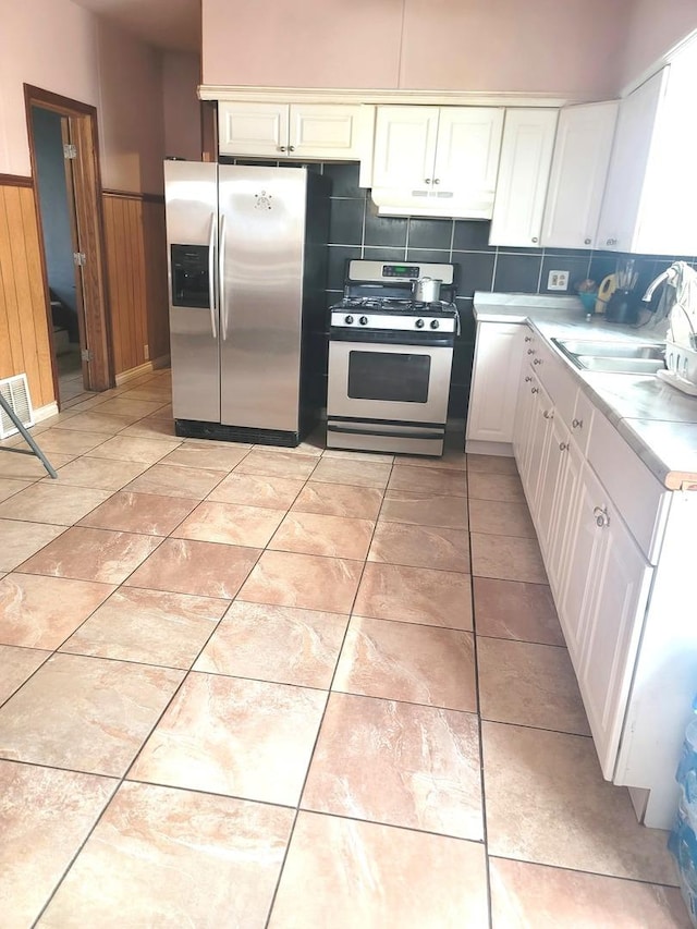 kitchen with light countertops, a wainscoted wall, a sink, white cabinets, and appliances with stainless steel finishes