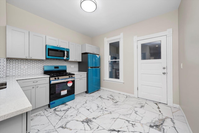 kitchen featuring baseboards, decorative backsplash, freestanding refrigerator, stainless steel gas stove, and marble finish floor
