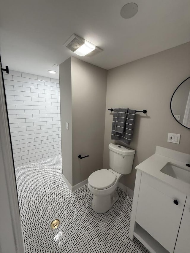 full bath featuring baseboards, vanity, toilet, and tiled shower