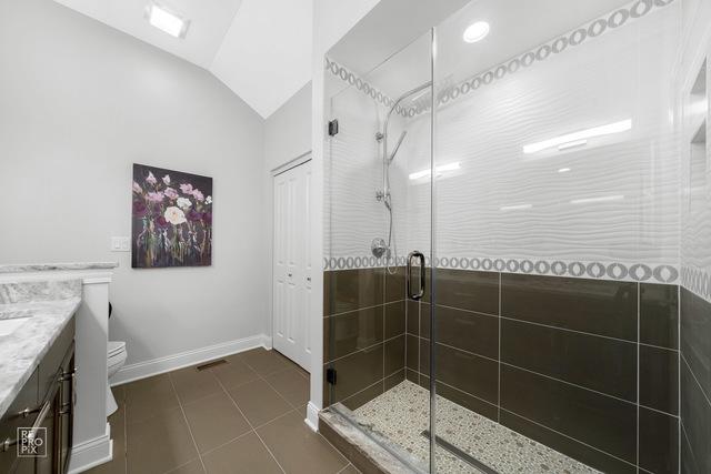 full bathroom with vanity, baseboards, lofted ceiling, a stall shower, and toilet