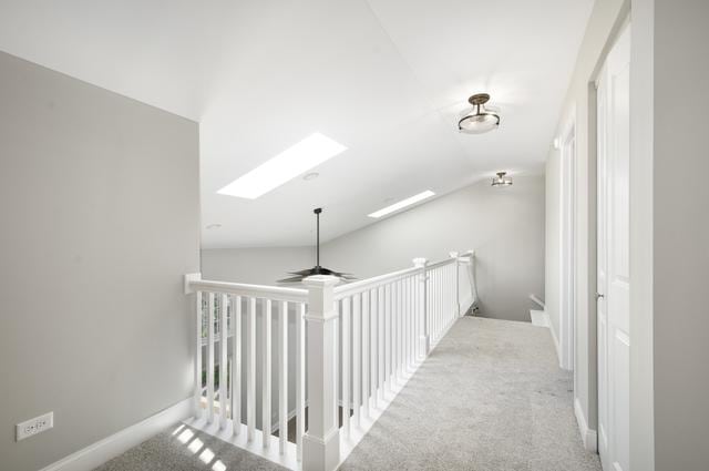 hall featuring lofted ceiling with skylight, an upstairs landing, baseboards, and carpet floors