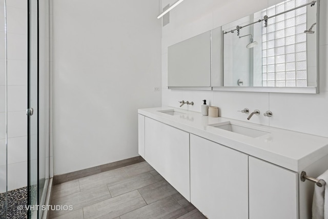 bathroom with baseboards, double vanity, a sink, and a stall shower