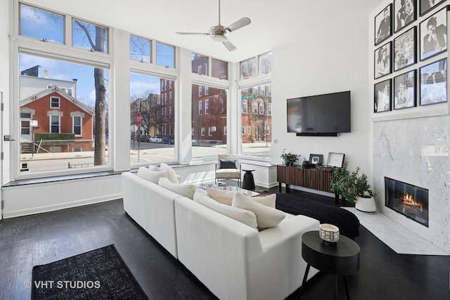 living area featuring baseboards, dark wood-style flooring, a premium fireplace, and a ceiling fan