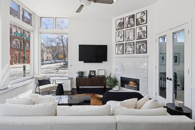 living area with a high end fireplace, a ceiling fan, french doors, and wood finished floors