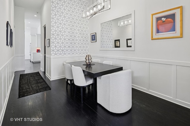 dining room featuring wainscoting, a decorative wall, and dark wood finished floors
