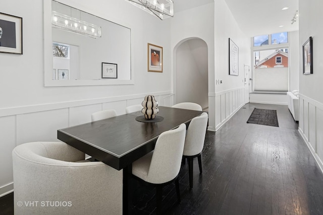 dining space featuring a wainscoted wall, dark wood-style floors, arched walkways, and a healthy amount of sunlight