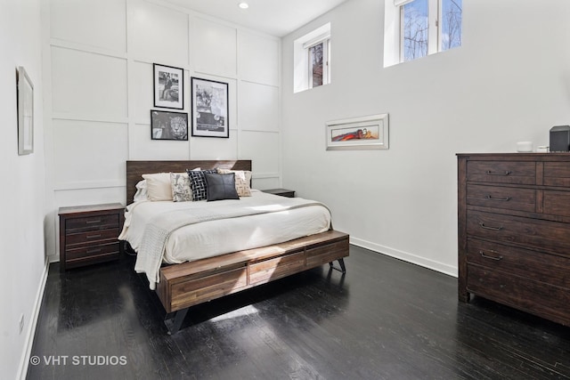 bedroom featuring dark wood-type flooring, a decorative wall, and baseboards