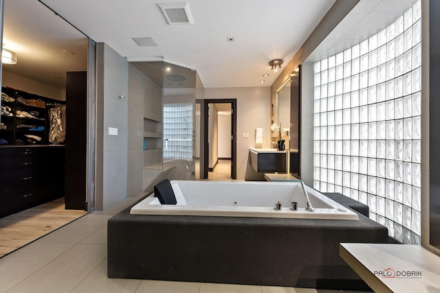 bathroom with tile patterned floors, visible vents, vanity, a tub with jets, and a spacious closet
