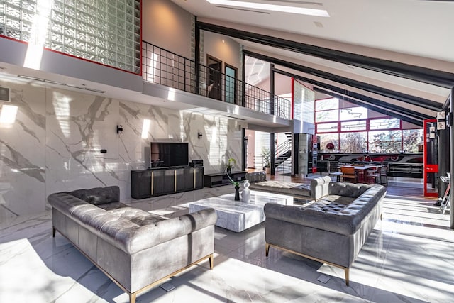 living area with stone wall, stairway, marble finish floor, and a towering ceiling