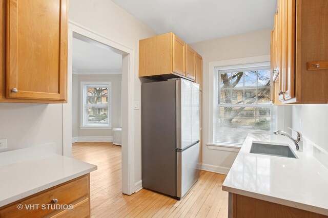 kitchen with baseboards, light wood-style flooring, light countertops, freestanding refrigerator, and a sink