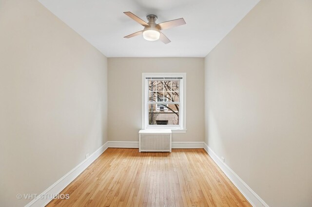 empty room featuring light wood-style flooring, a ceiling fan, radiator, and baseboards