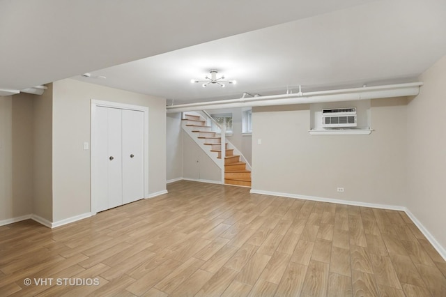 basement with baseboards, light wood finished floors, a wall mounted AC, and stairs