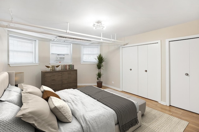 bedroom featuring baseboards, light wood finished floors, cooling unit, and two closets