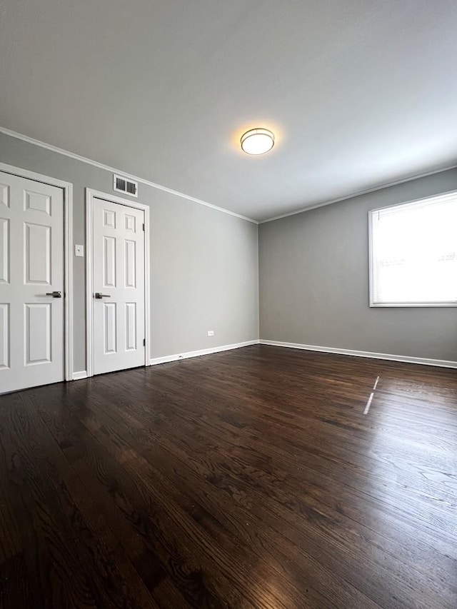 unfurnished bedroom featuring baseboards, visible vents, two closets, and dark wood-type flooring