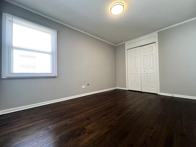 unfurnished bedroom featuring baseboards, dark wood-style flooring, a closet, and crown molding