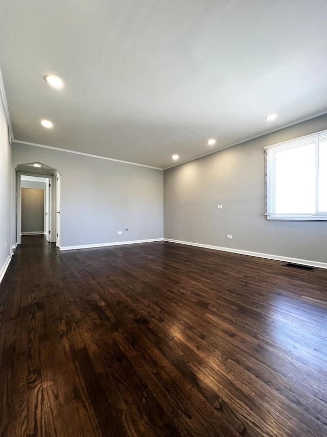 empty room featuring arched walkways, baseboards, and dark wood finished floors