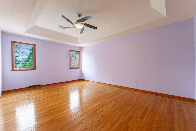 spare room featuring light wood-style floors, a ceiling fan, a tray ceiling, and visible vents