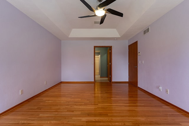 spare room featuring a tray ceiling, visible vents, ceiling fan, and light wood-style floors