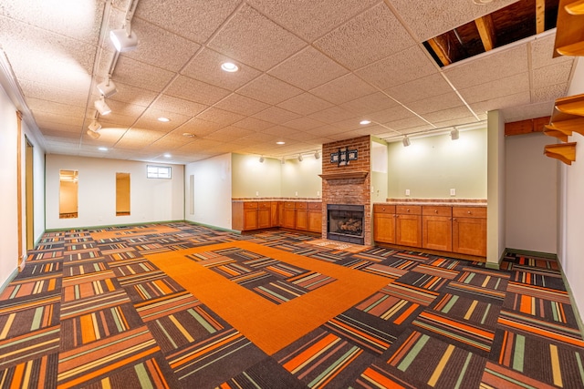finished basement with carpet floors, track lighting, and a brick fireplace
