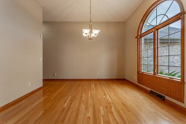 spare room featuring baseboards, visible vents, light wood-type flooring, and a notable chandelier