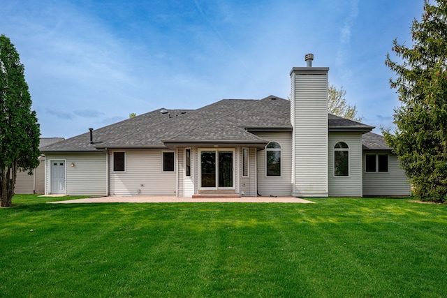 back of house with a yard, roof with shingles, a chimney, and a patio area