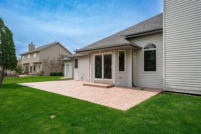 rear view of house with a lawn, a shingled roof, and a patio area