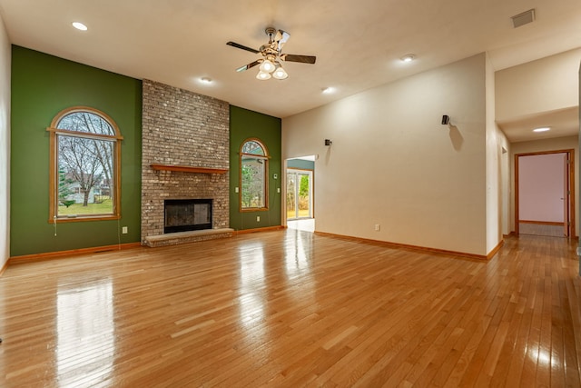 unfurnished living room with a high ceiling, light wood finished floors, a ceiling fan, baseboards, and visible vents
