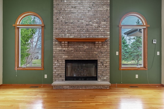 unfurnished living room featuring baseboards, visible vents, wood finished floors, and a fireplace