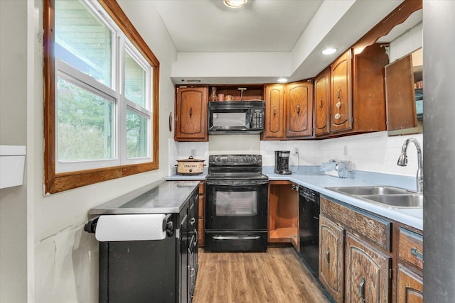 kitchen with light countertops, a sink, light wood-style flooring, black appliances, and decorative backsplash