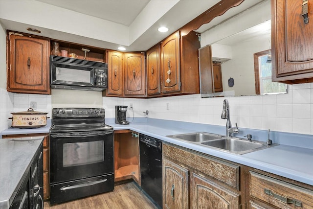 kitchen featuring light countertops, backsplash, a sink, light wood-style flooring, and black appliances