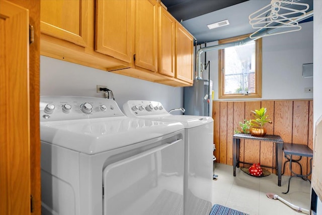 washroom with water heater, wood walls, visible vents, cabinet space, and washing machine and clothes dryer