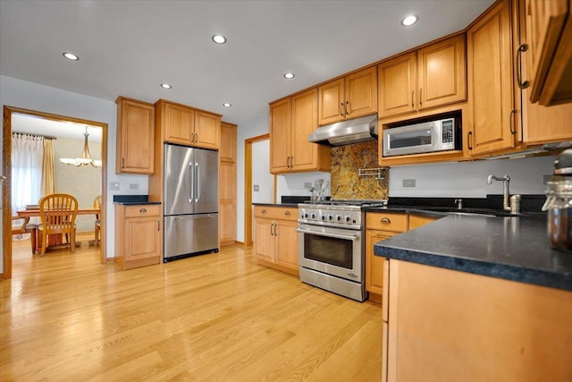 kitchen featuring light wood-type flooring, under cabinet range hood, dark countertops, a sink, and stainless steel appliances