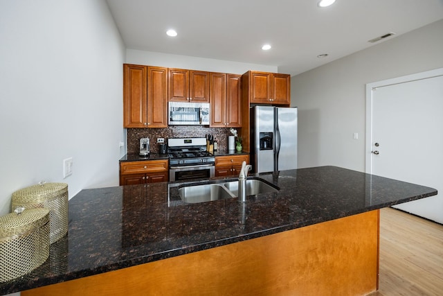 kitchen with stainless steel appliances, backsplash, light wood finished floors, a sink, and visible vents