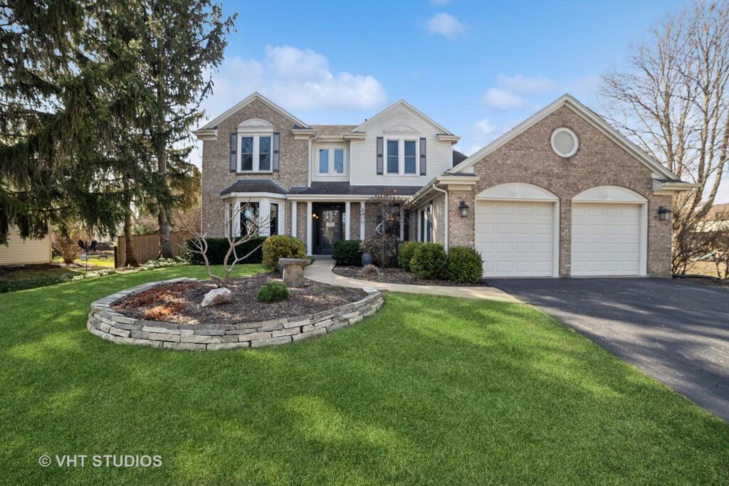 1604 Lilac Dr, Crystal Lake, IL 60014 - traditional home with driveway, brick siding, an attached garage, and a front yard