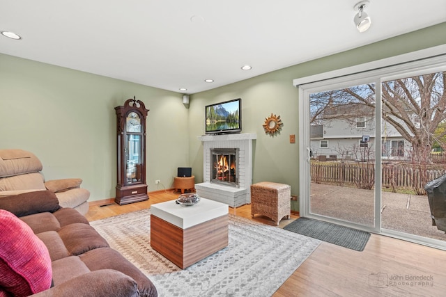 living room featuring recessed lighting, a fireplace, light wood-type flooring, and baseboards