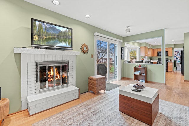 living area featuring a brick fireplace, recessed lighting, and light wood-type flooring