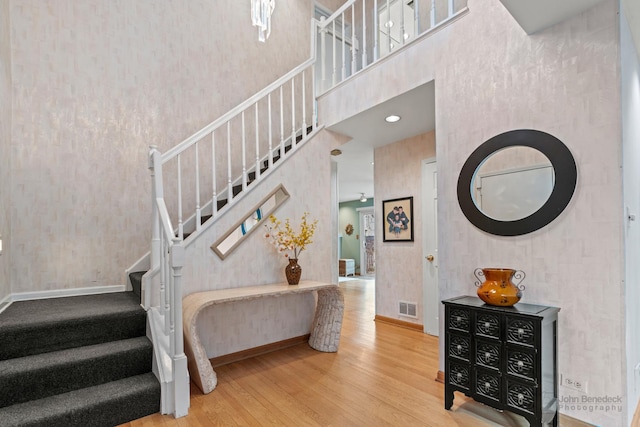 stairway with visible vents, wallpapered walls, baseboards, a towering ceiling, and wood finished floors