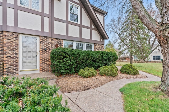 property entrance with brick siding, stucco siding, and a lawn
